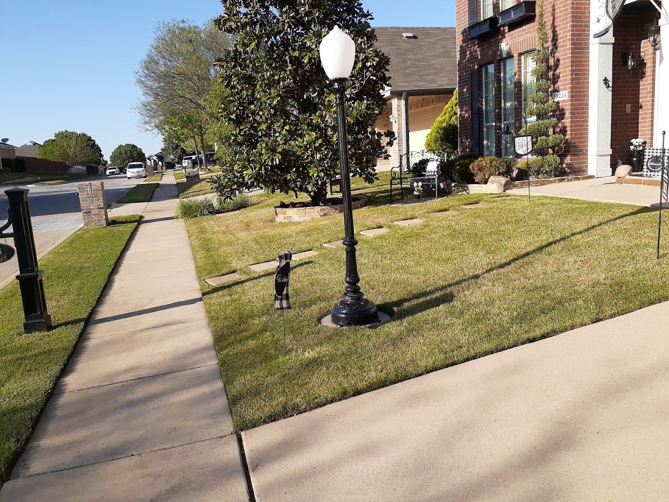 Sidewalk next to lawn with black lamppost and brick house on sunny day.