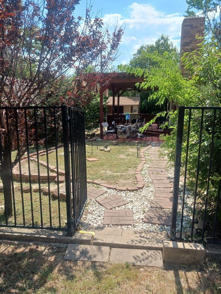 Open black gate leads to backyard with stepping stones, lawn, and a pergola.