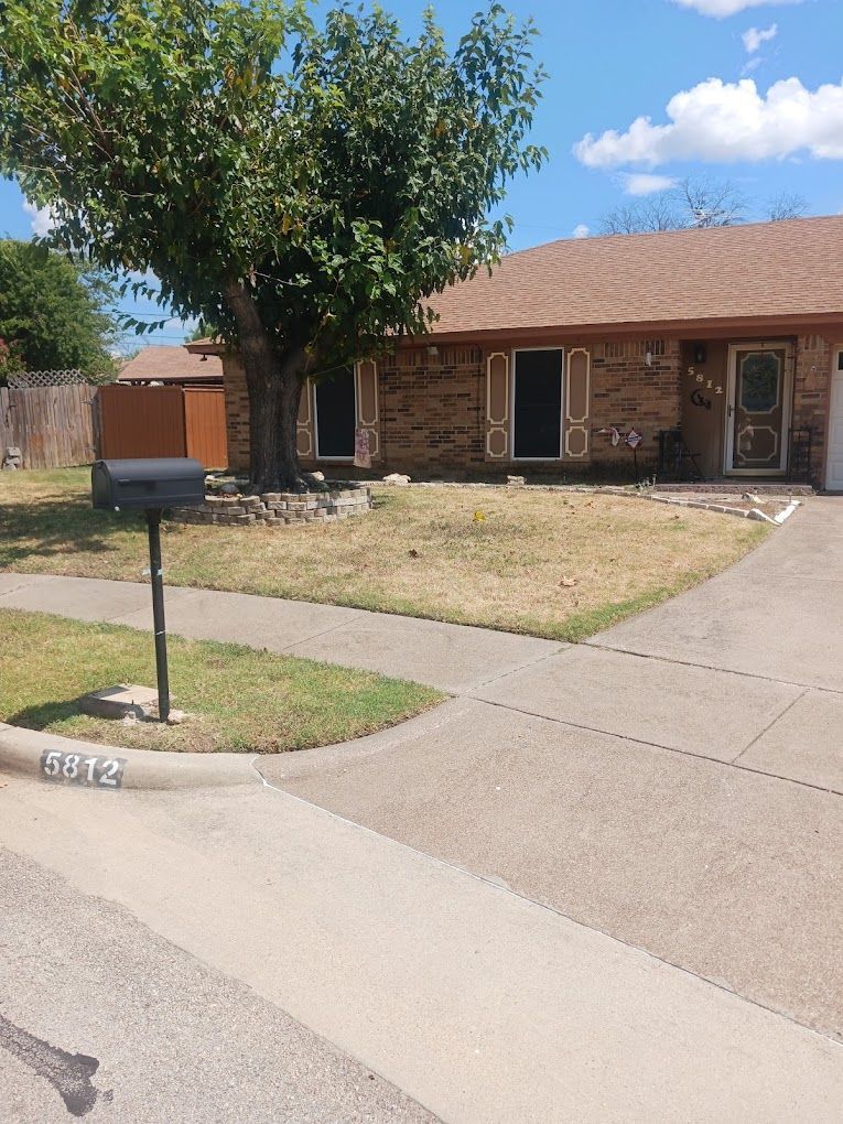 House with a brown roof and brick exterior, partial lawn, tree, and mailbox on the front.