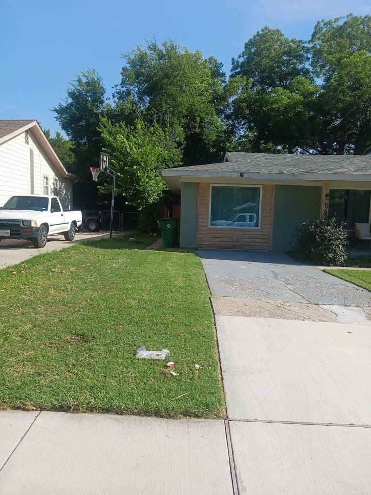 A residential exterior with green lawn, driveway, and a light-colored house under a clear sky.