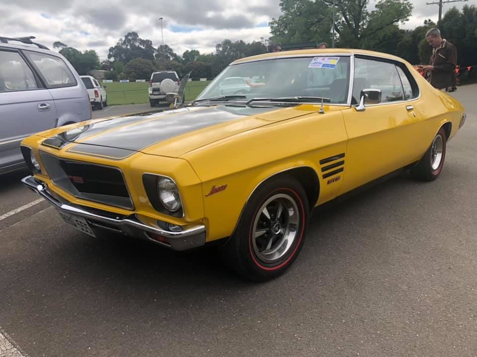 Yellow vintage Holden Torana car with black hood stripe, parked outdoors.