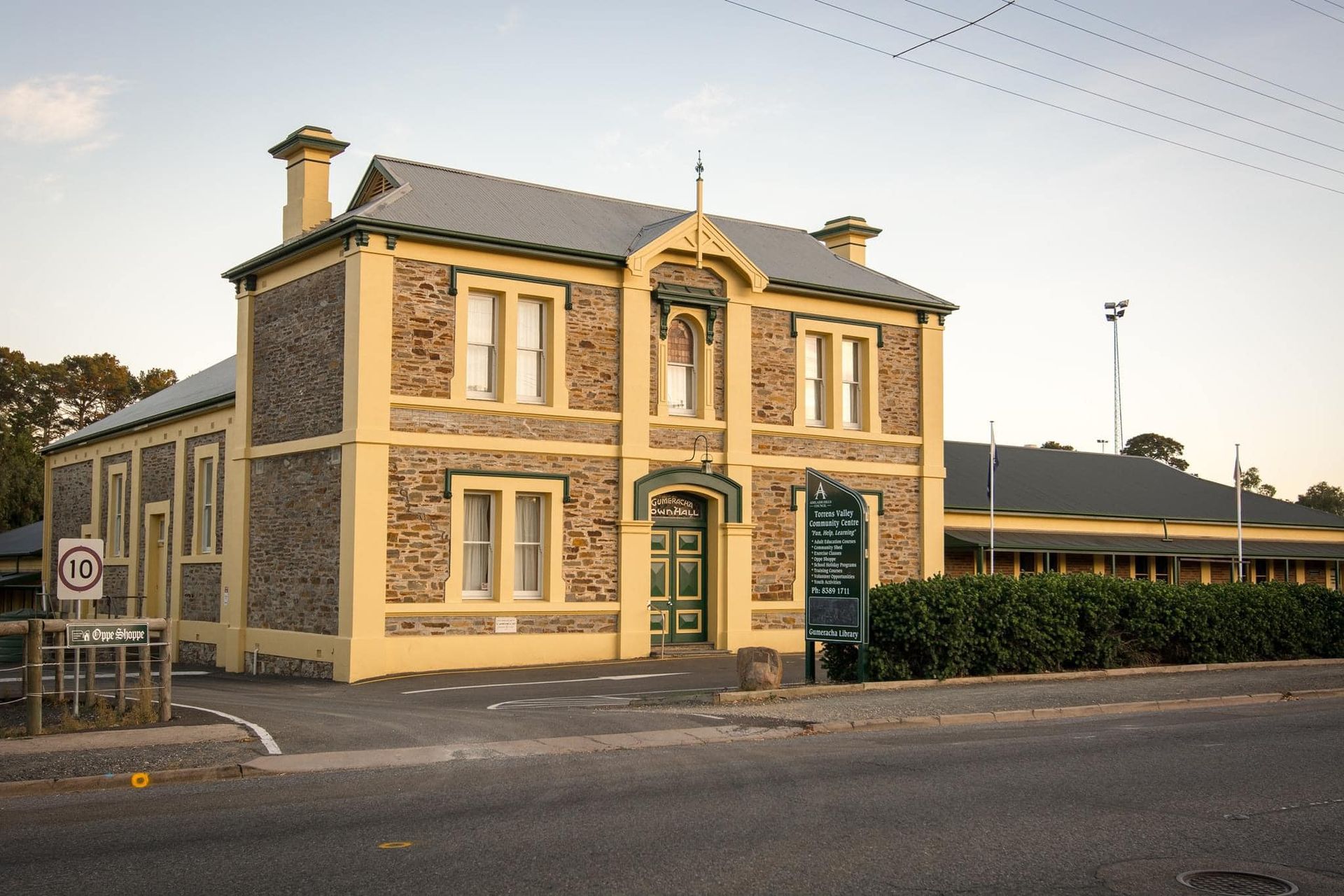 Stone building with yellow trim, possibly a community hall, with a sign and street sign visible.