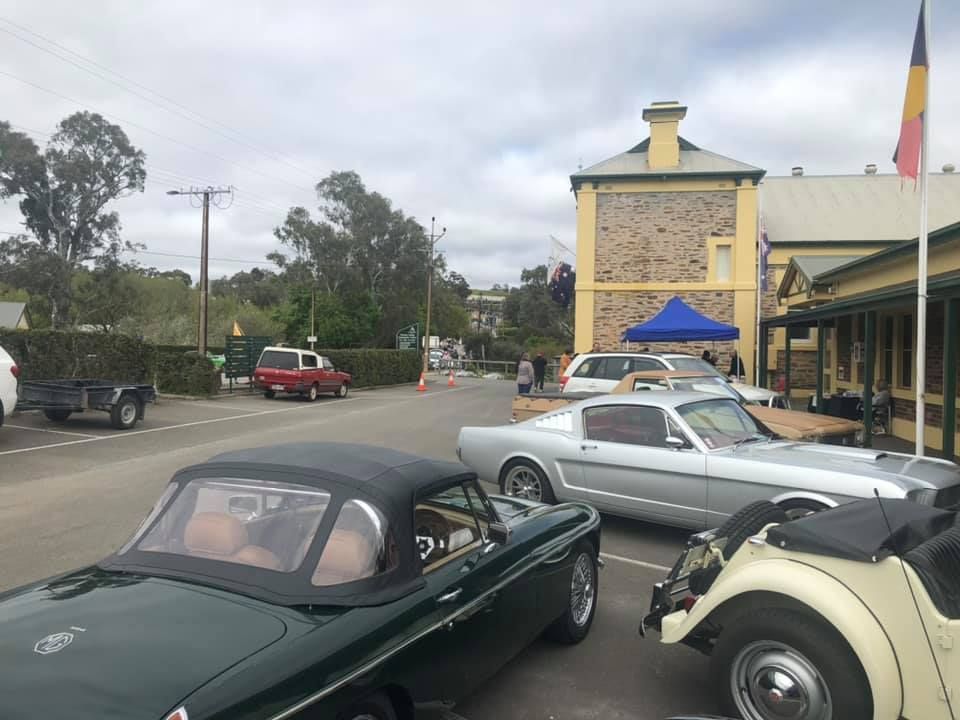 Classic cars parked outside a building with a flag; sky overhead.