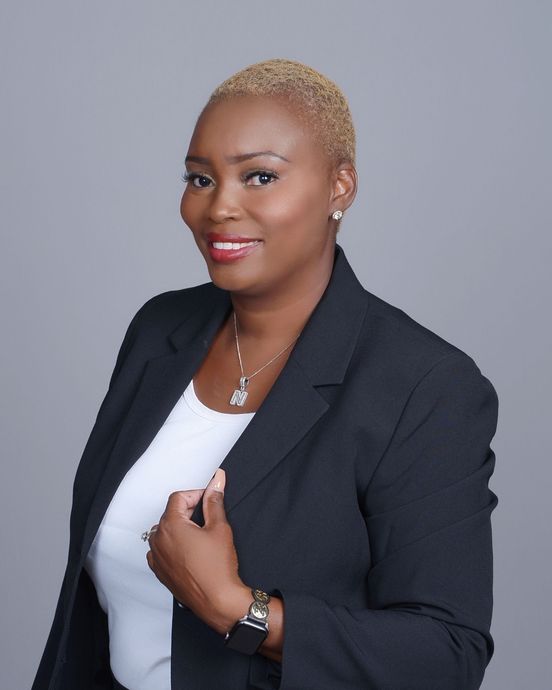 A woman is sitting at a desk with a laptop and a vase of flowers.