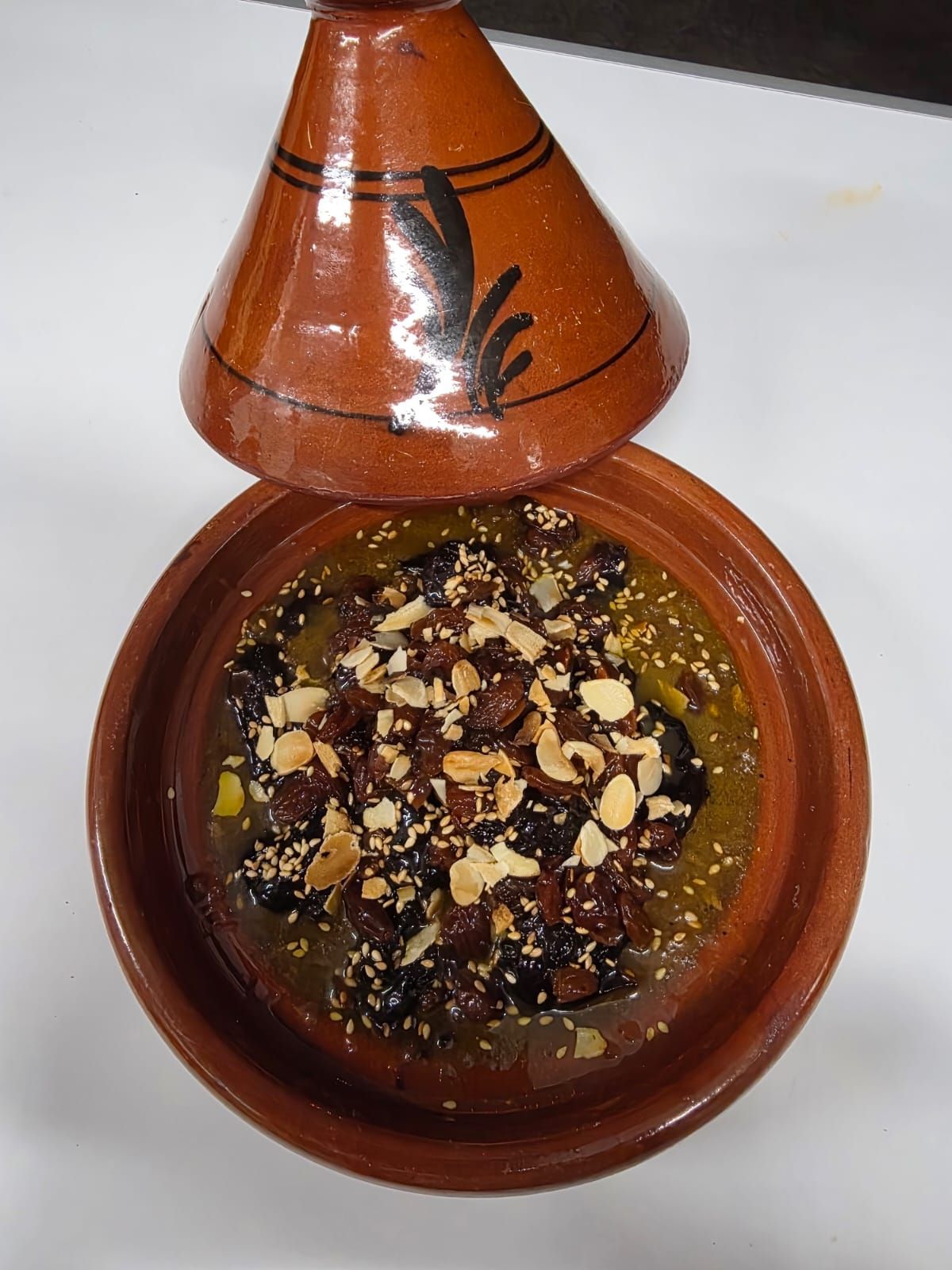 Tajine avec couvercle, contenant un ragoût aux noix et garniture, en faïence brune.