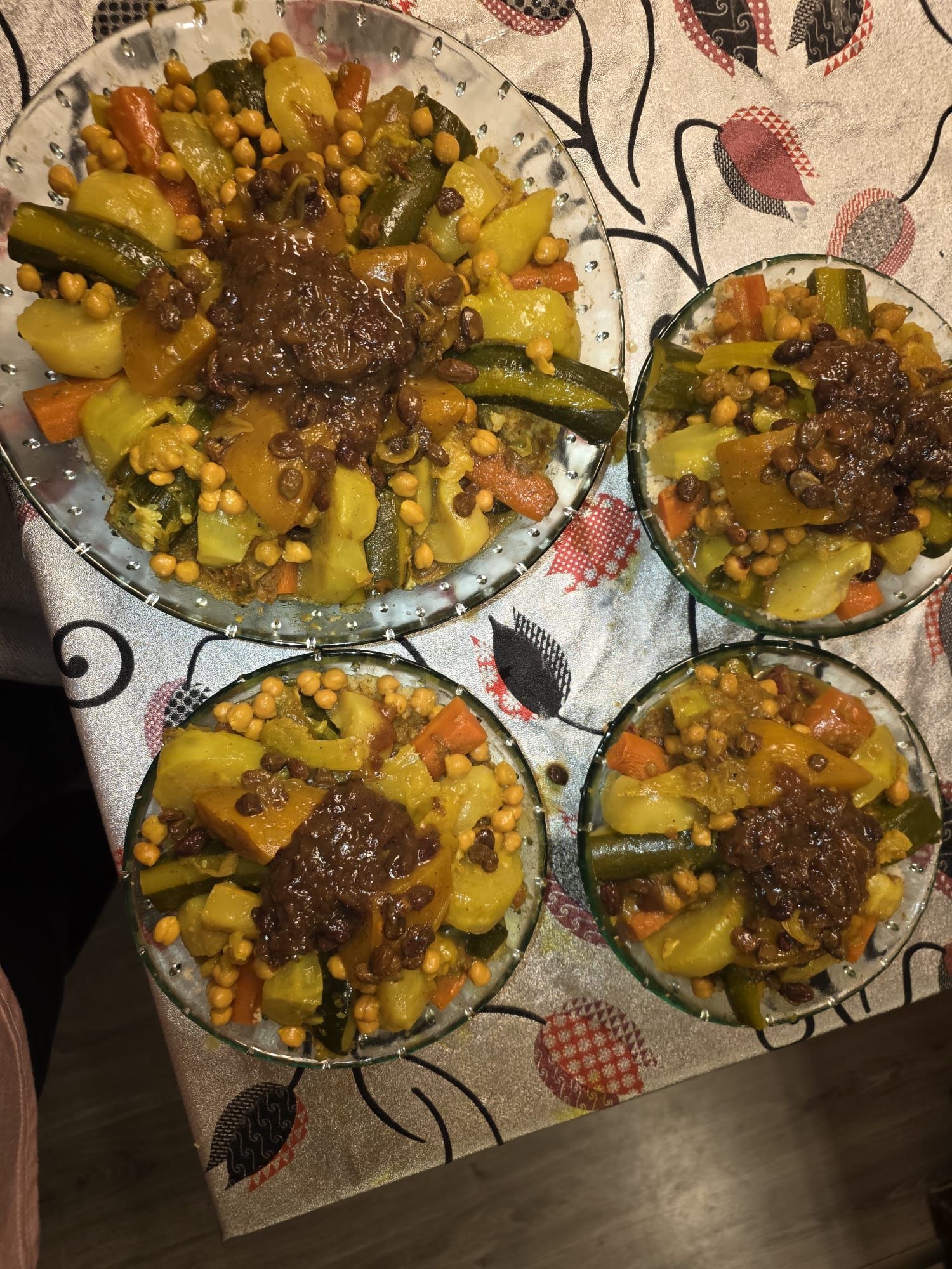 Quatre assiettes de ragoût de légumes aux pois chiches et à la sauce brune, servies sur une nappe à motifs.