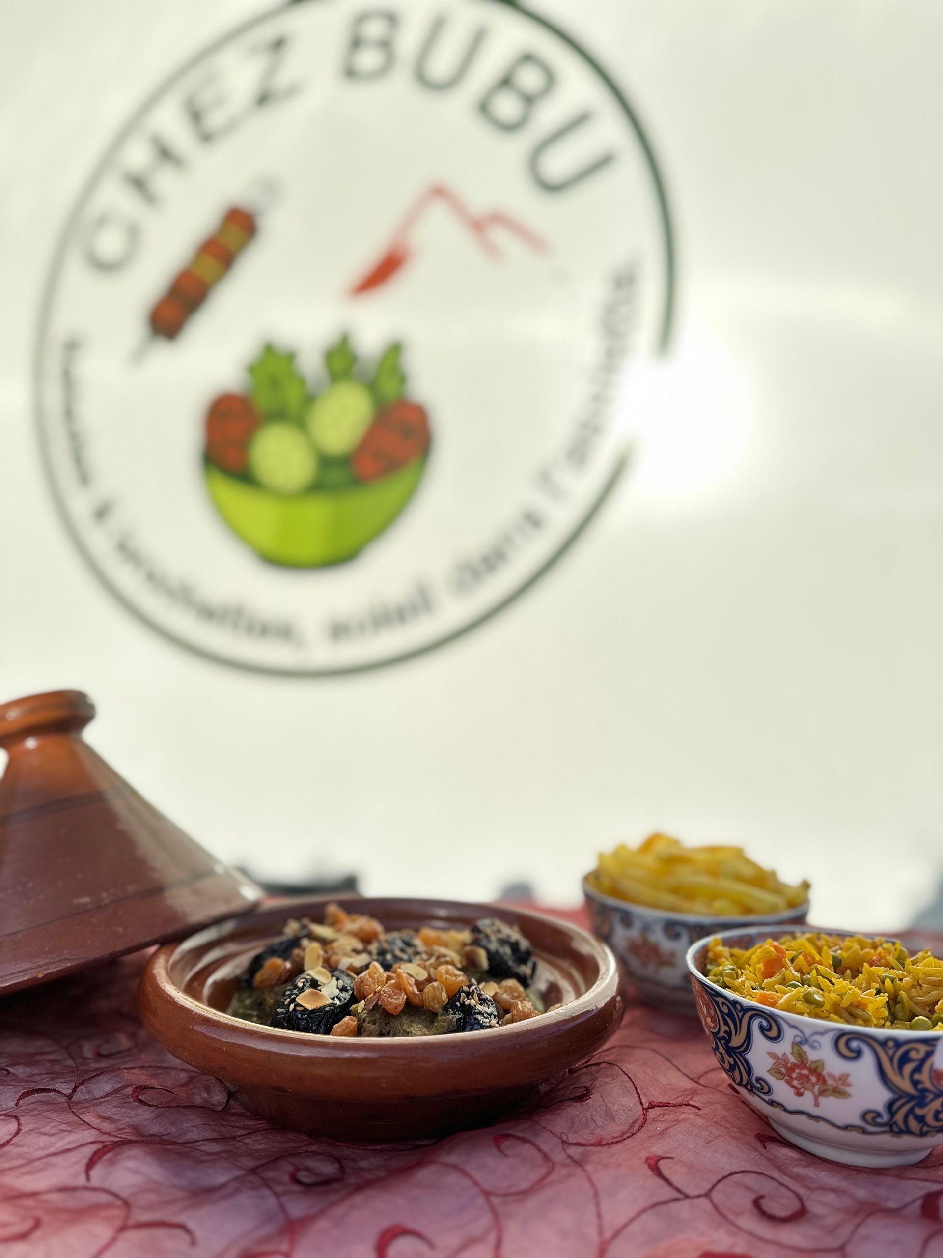 Tajine brun contenant des aliments, des petits accompagnements et un logo portant l'inscription « Chez Bubu ».