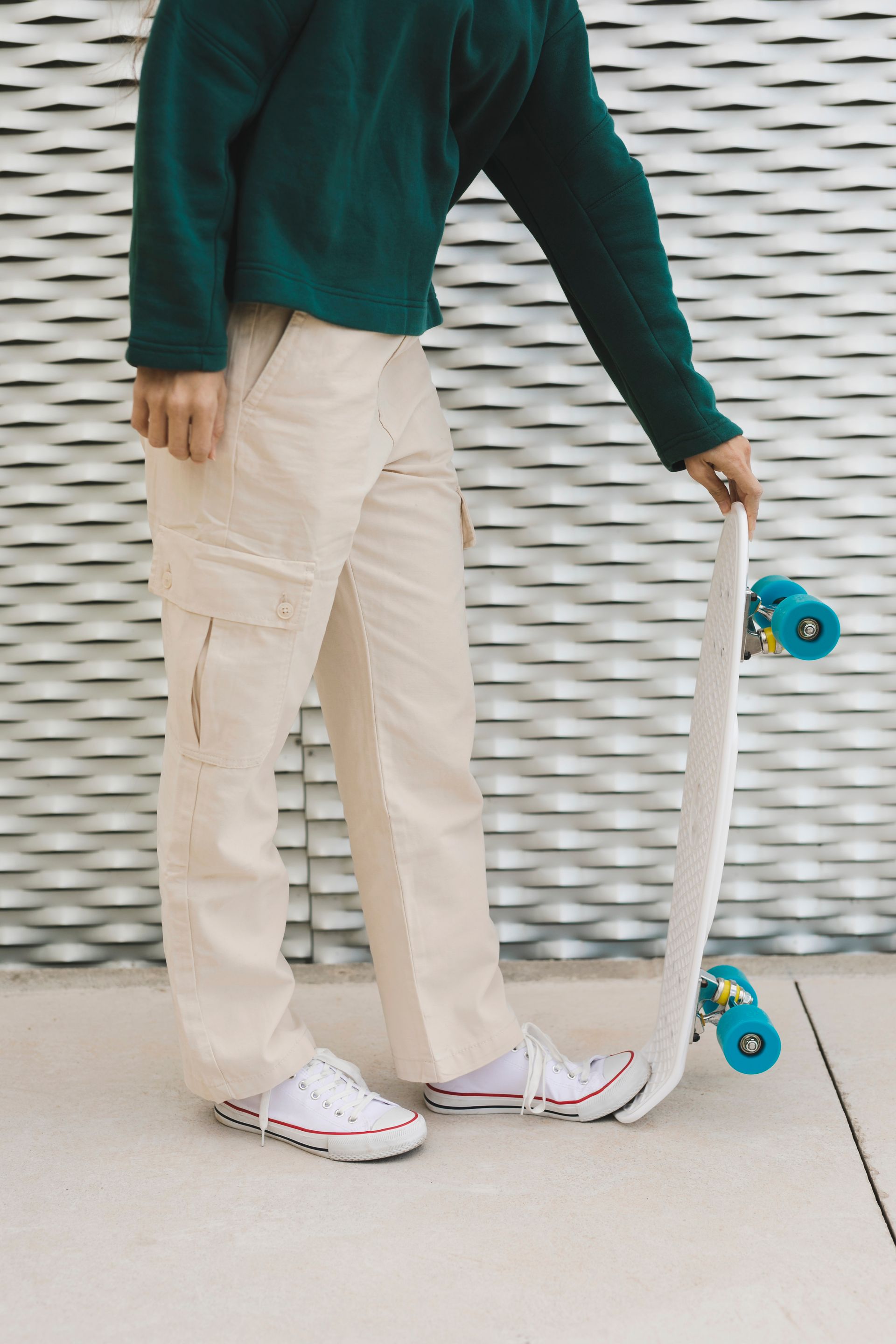 Persona con suéter verde y pantalones beige sosteniendo una patineta blanca con ruedas azules