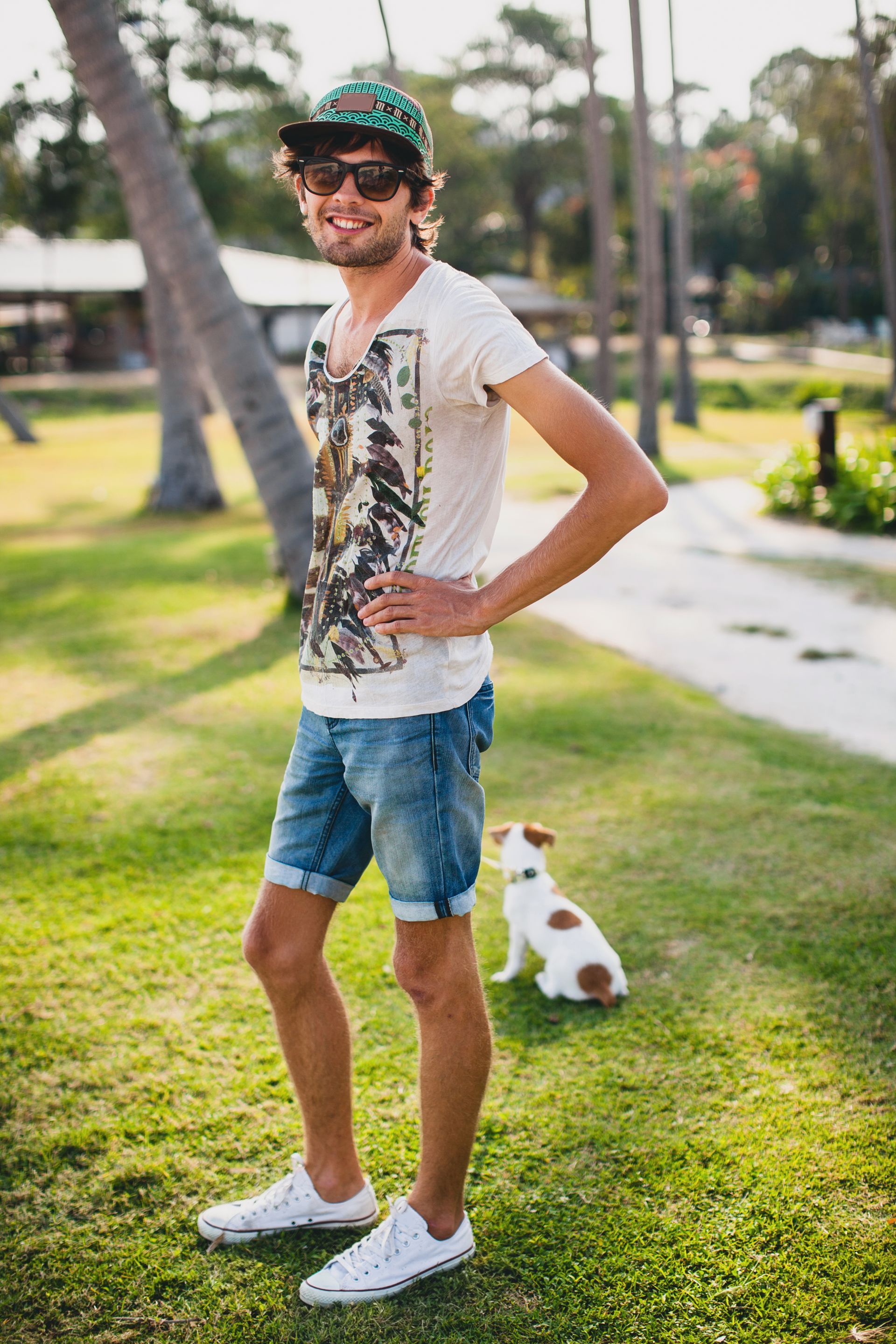 Un hombre con gafas de sol, gorra de béisbol y pantalones cortos está de pie sobre el césped