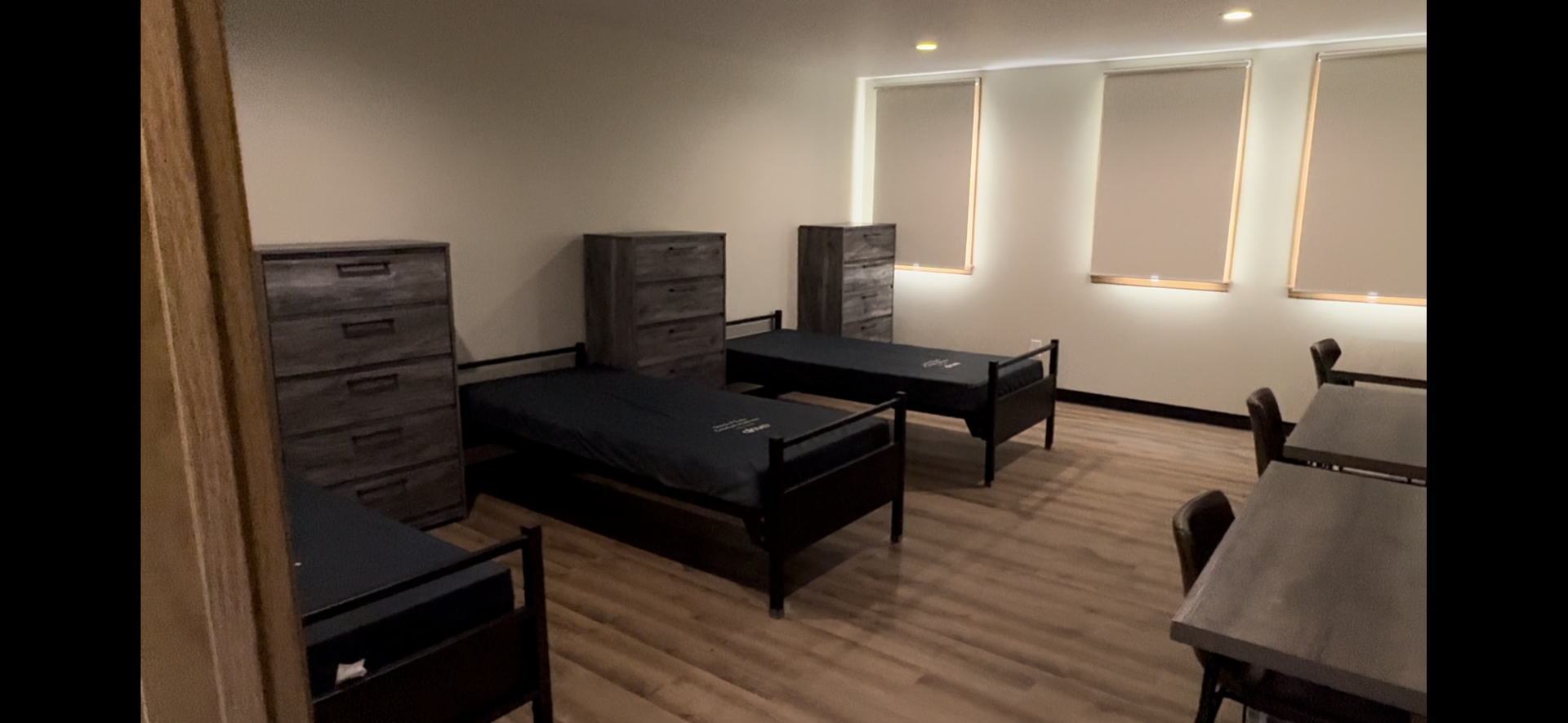 A room with three beds , dressers , chairs and a table.