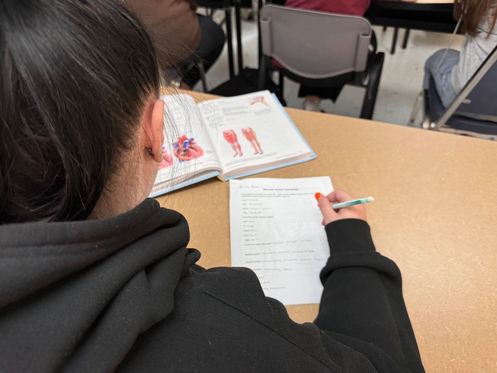A girl is sitting at a table with a book and a piece of paper