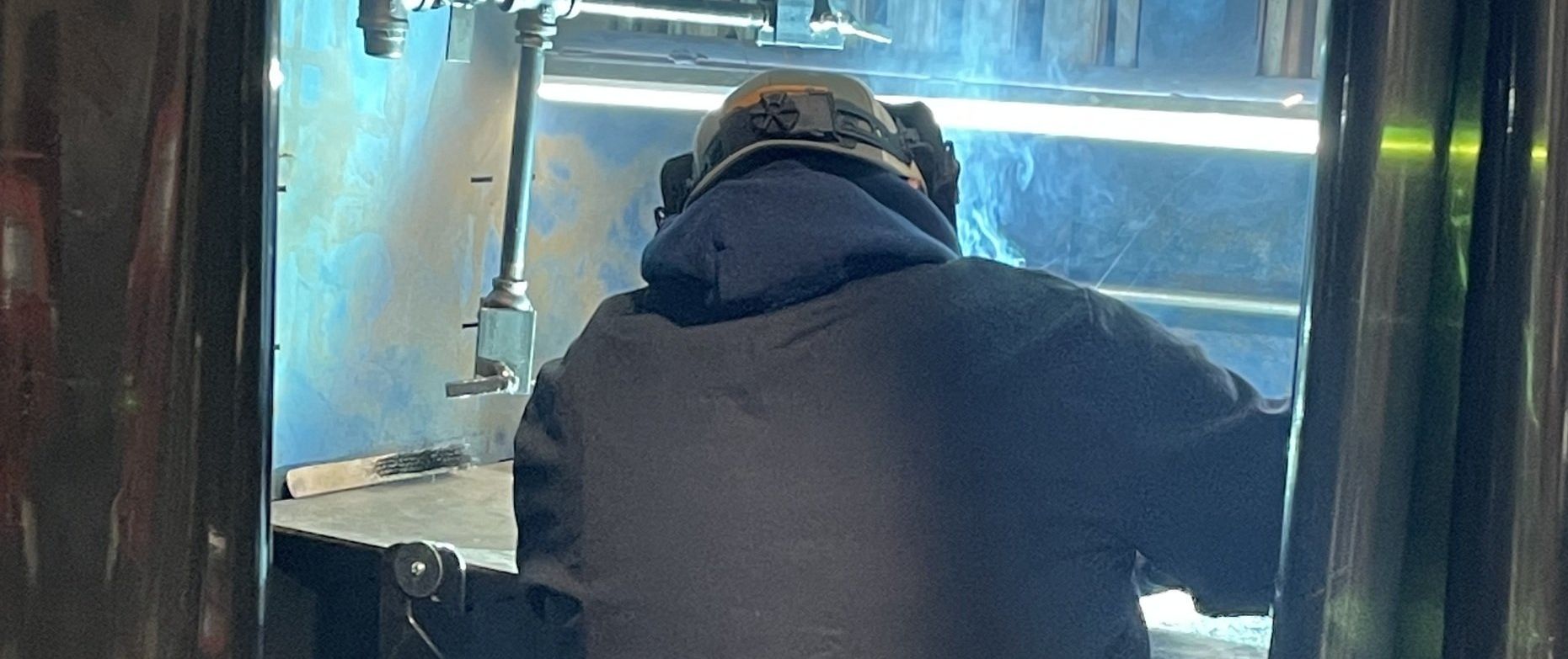 A man is welding a piece of metal in a factory.