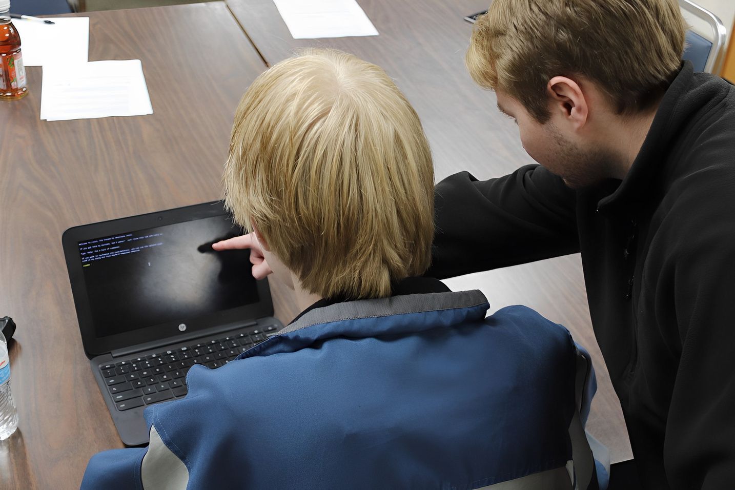 Two men are looking at a laptop and one is pointing at the screen