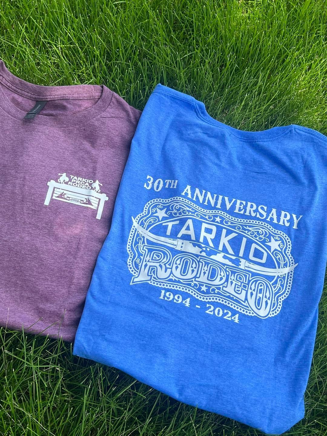 Two t-shirts are sitting on top of a lush green field.