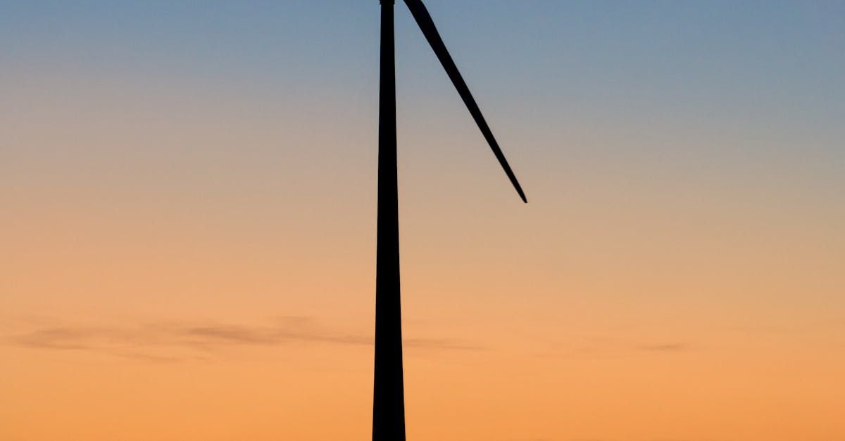 A wind turbine is silhouetted against a sunset sky.