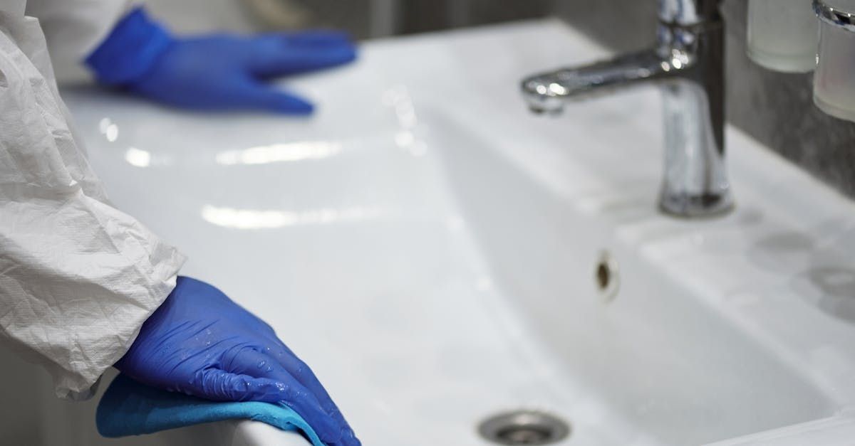 A person wearing blue gloves is cleaning a bathroom sink.