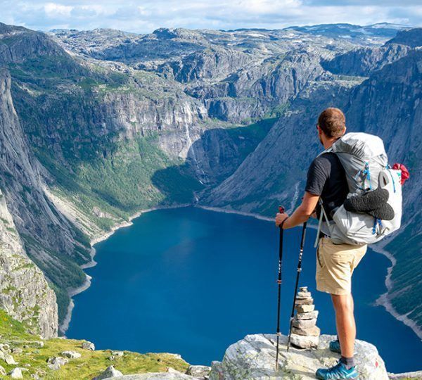 A man with a backpack is standing on top of a mountain overlooking a lake.