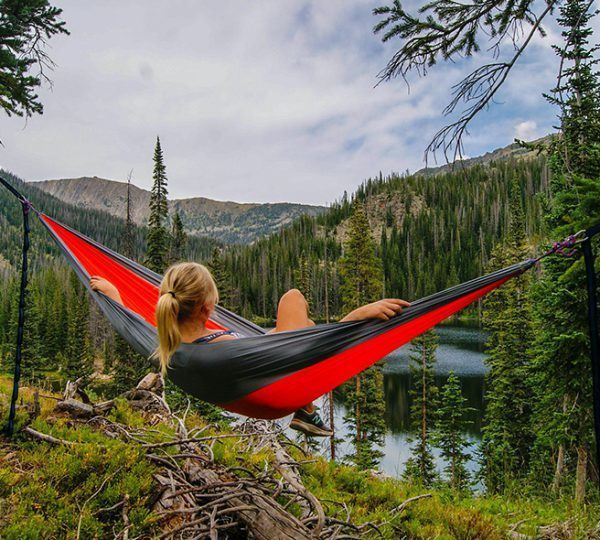 A woman is laying in a hammock overlooking a lake.