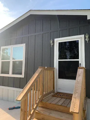Gray-sided house with wooden steps, white door, and a window. Sunny day.
