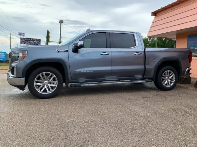 Gray GMC Sierra truck parked on a paved lot beside a building with a pink exterior.