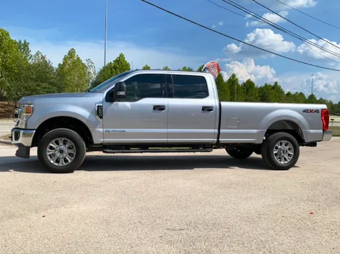 Silver Ford F-250 pickup truck with 4x4 emblem, parked on pavement, with a partly cloudy sky.