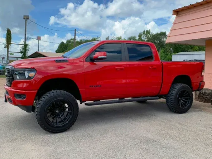 Red lifted Ram truck with black wheels parked near a building on a sunny day.