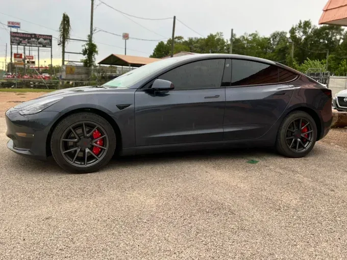 Dark gray Tesla Model 3 with tinted windows and red brake calipers parked outside.