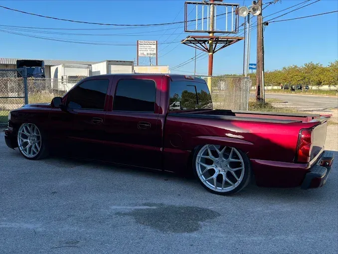 Red lowered pickup truck with tinted windows and custom wheels parked on asphalt.