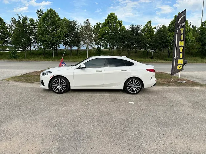 White BMW sedan parked outside a tinting shop on a sunny day.