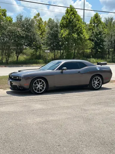 Gray Dodge Challenger parked on an asphalt road; trees and sky in the background.