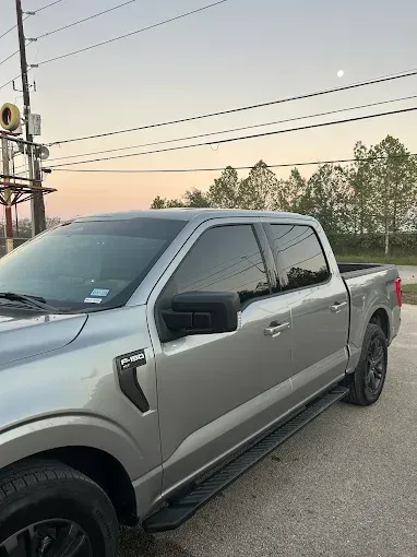 Silver Ford F-150 pickup truck parked outdoors at dusk with tinted windows, black wheels and running boards.