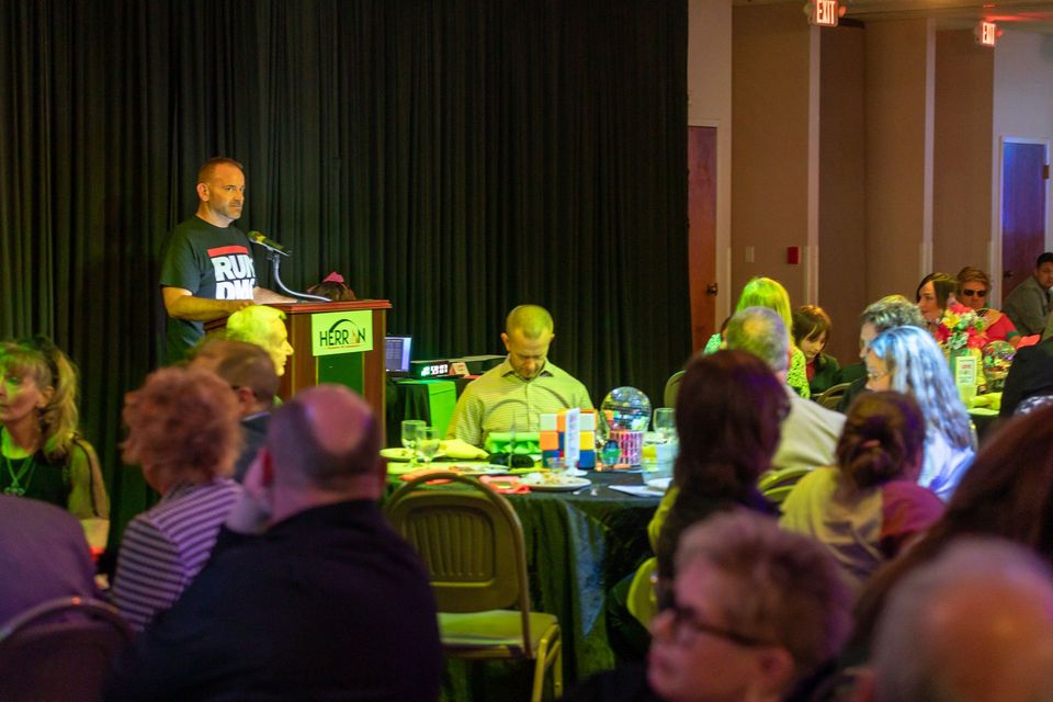 A man is giving a speech at a podium in front of a crowd of people sitting at tables.