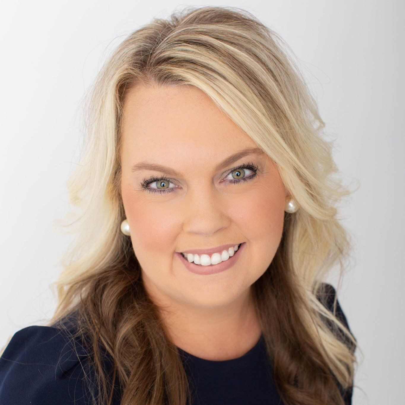 A woman with blonde hair and pearl earrings is smiling for the camera.