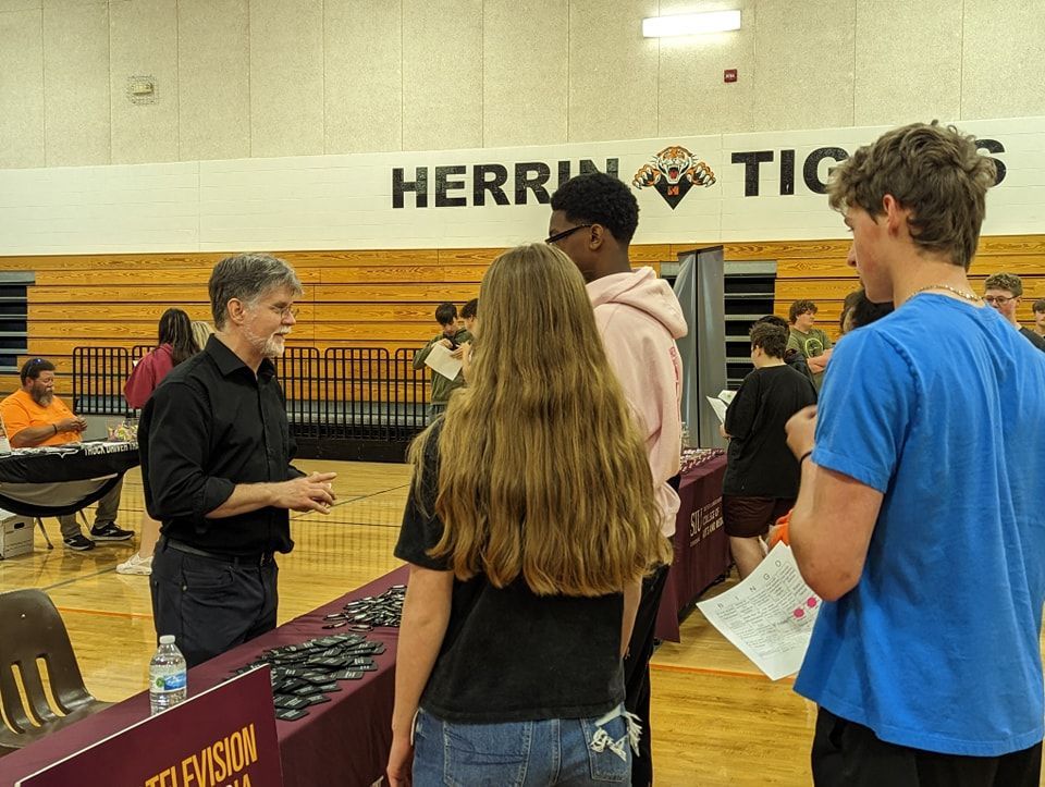 A group of people are standing around a table in a gym talking to a man.