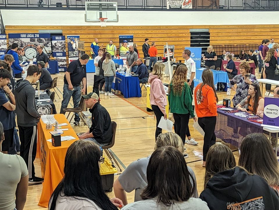 A large group of people are gathered in a gym at a job fair.