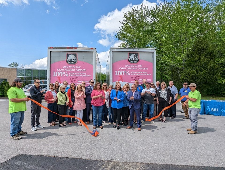 A group of people are cutting a ribbon in front of two trucks.