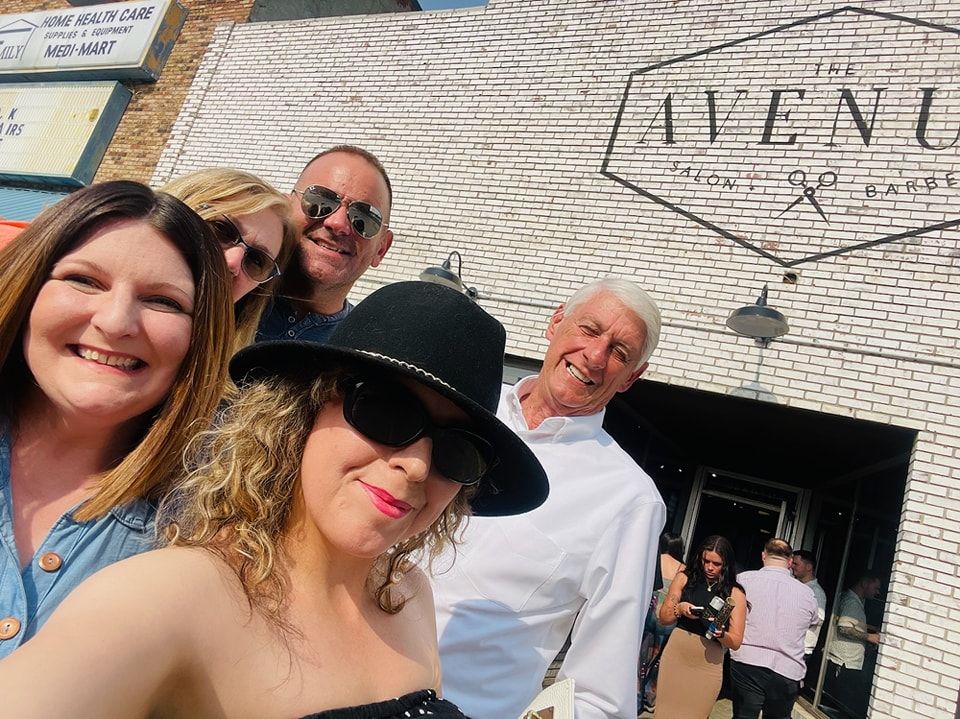 A group of people are posing for a picture in front of a building that says avenue