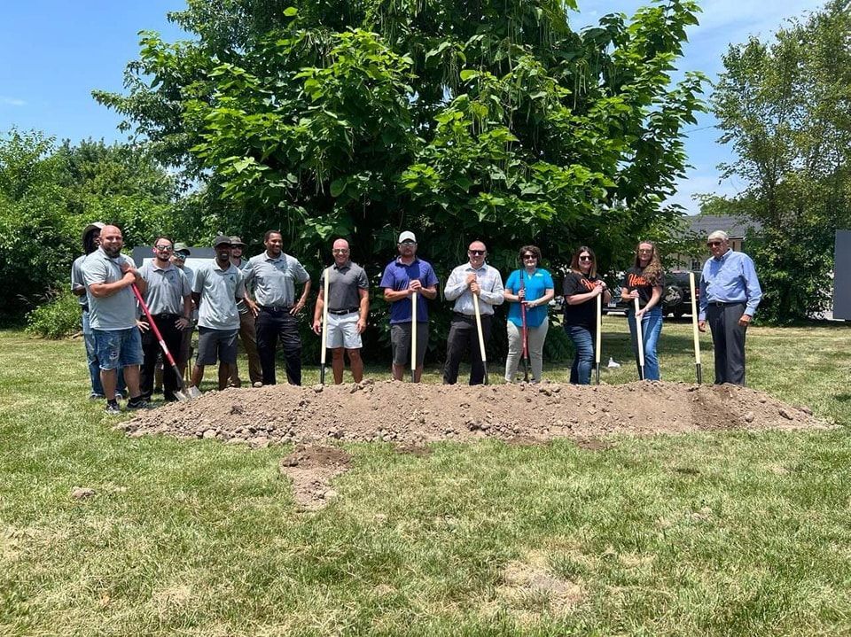 A group of people are standing in a dirt field holding shovels.