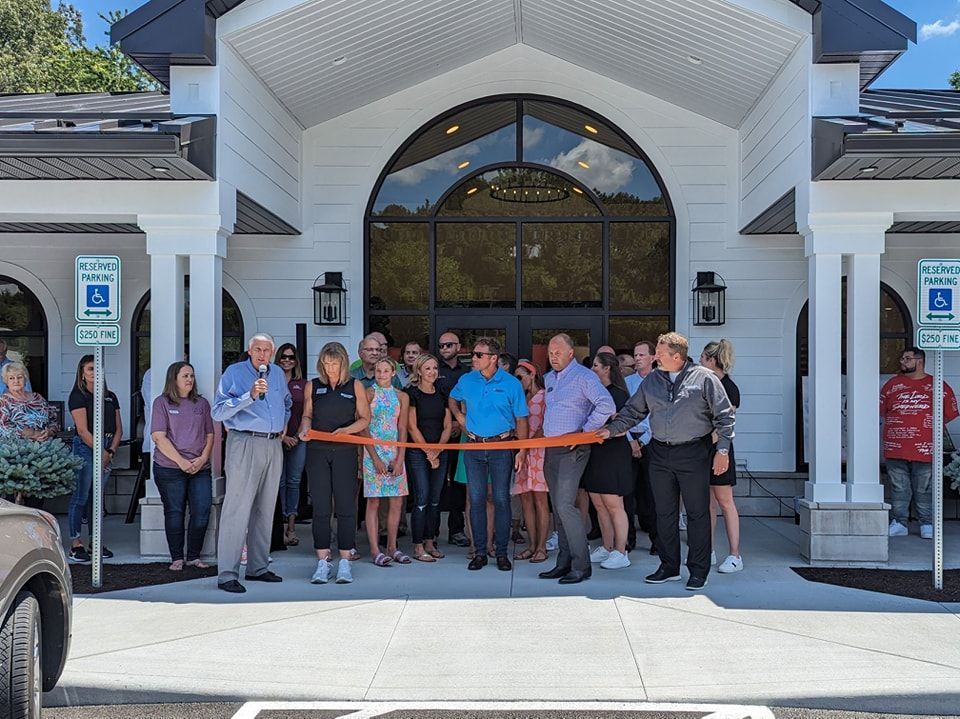 A group of people are standing in front of a building cutting a ribbon.