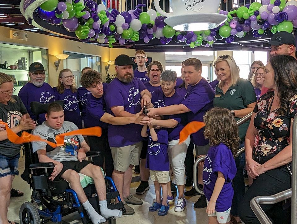 A group of people are standing around a man in a wheelchair cutting a ribbon.