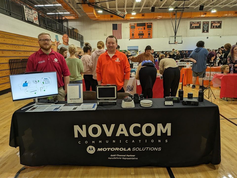 A group of people are standing around a table that says novacom on it