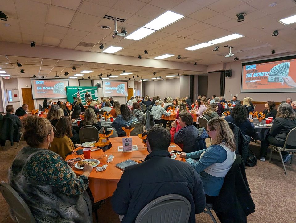 A large group of people are sitting at tables in a large room.