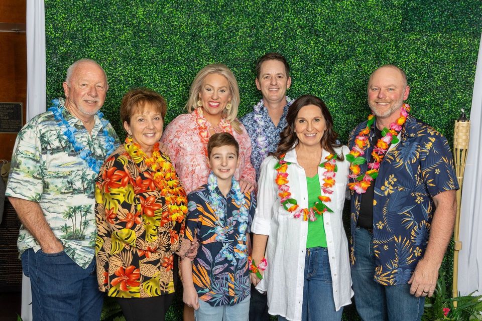 A group of people wearing hawaiian shirts and lei are posing for a picture.