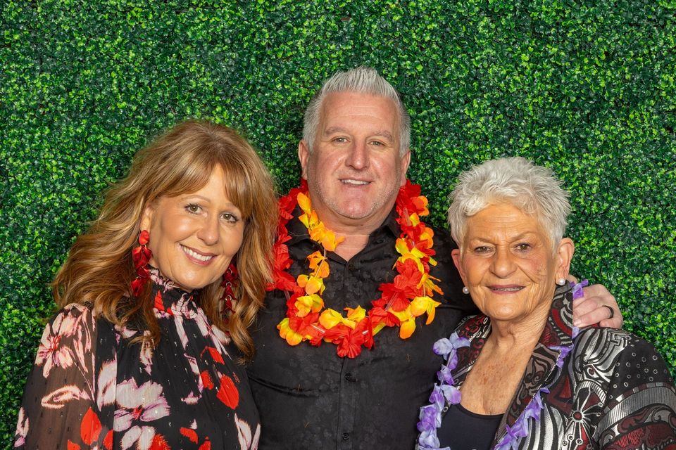 A man and two women are posing for a picture in front of a hedge wall.