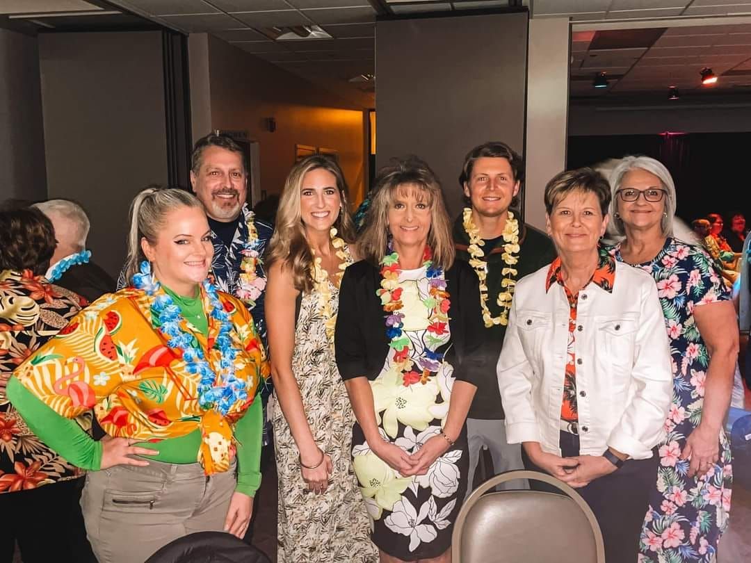 A group of people wearing hawaiian shirts and lei are posing for a picture.