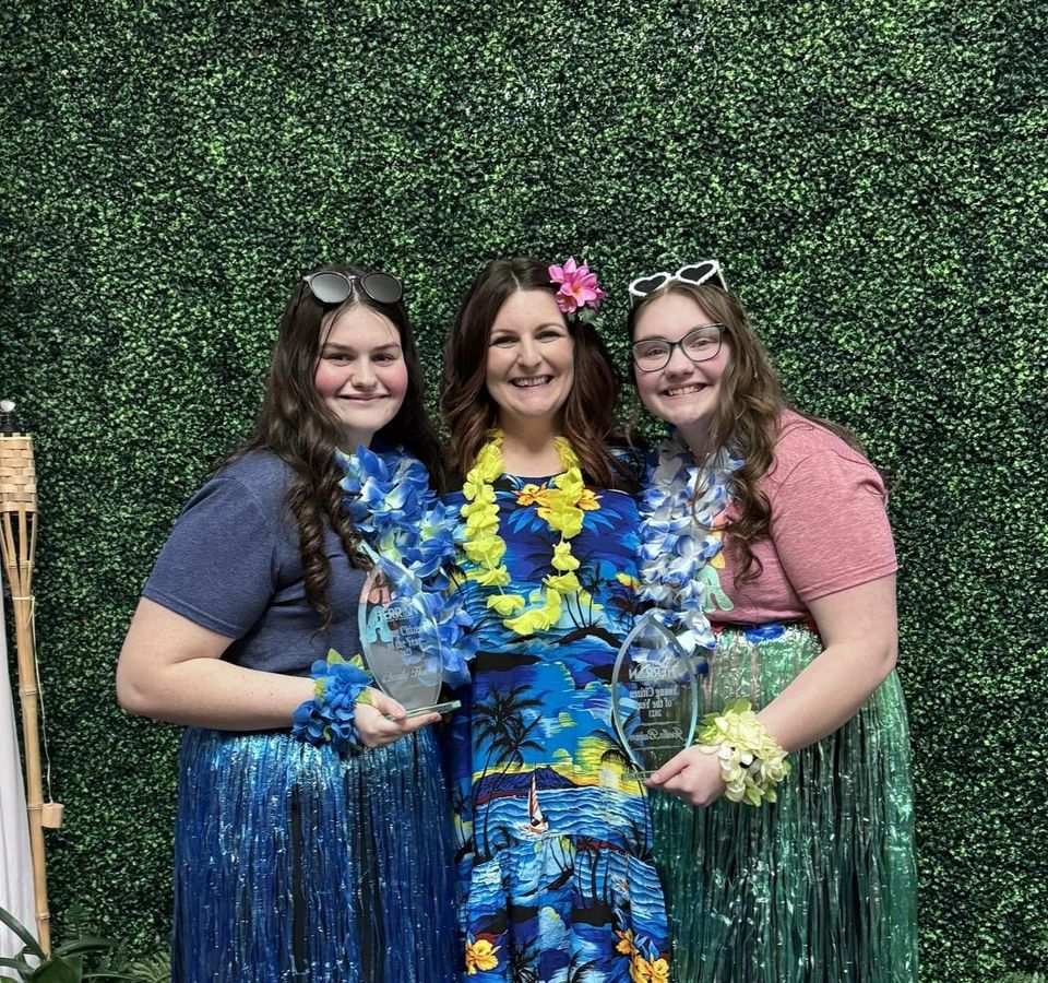 Three women dressed in hawaiian outfits are posing for a picture.