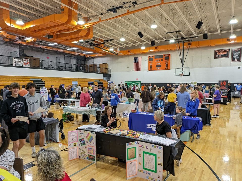 A large group of people are standing around tables in a gym.