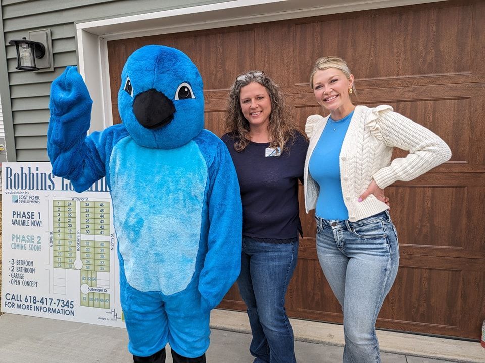 Two women standing next to a blue bird mascot