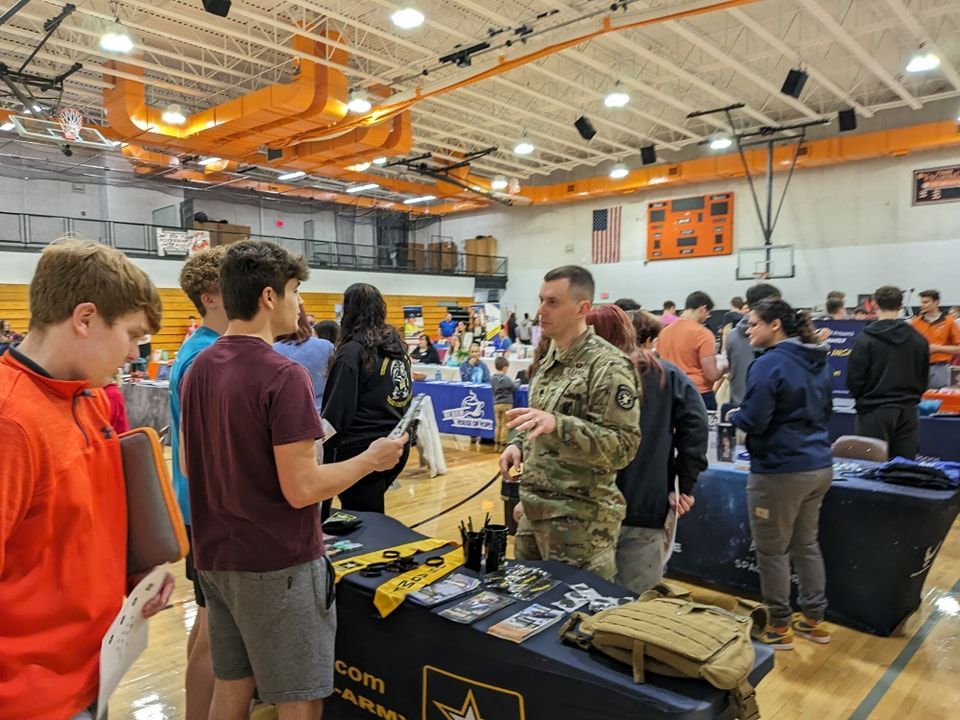 A man in a military uniform is talking to a group of people in a gym.