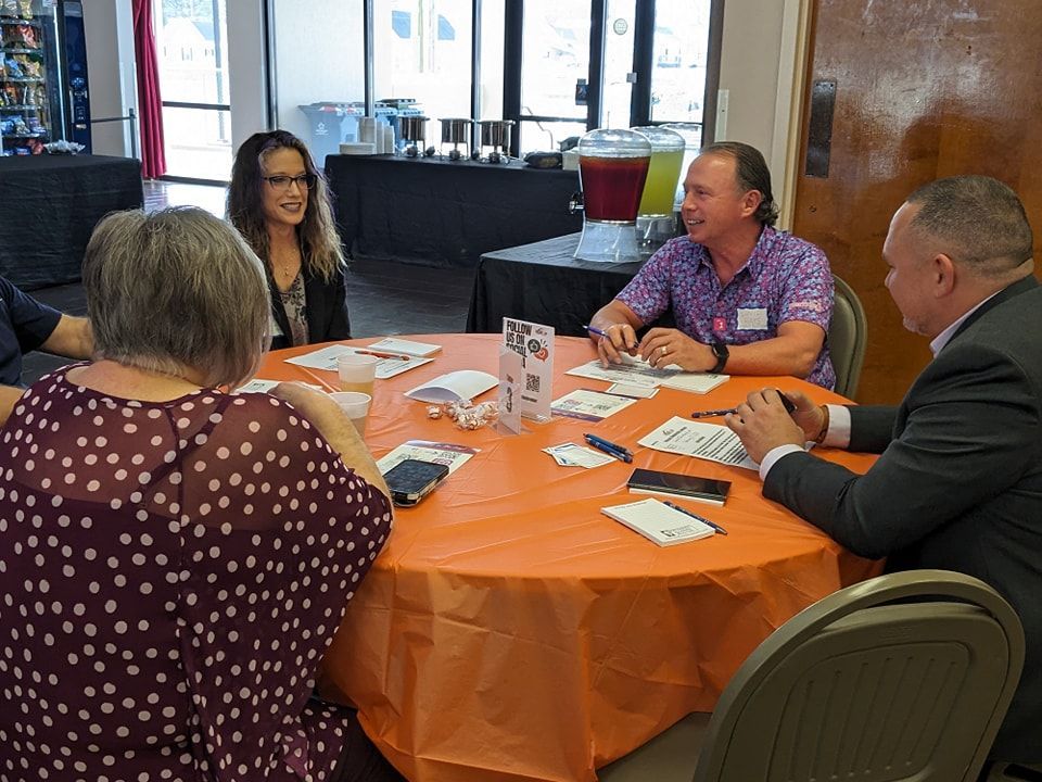 A group of people are sitting around a table with an orange tablecloth.